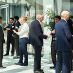 A group of suited employees from Societe Generale meet students in a corporate building filled with light.