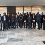 A large group of Black professionals standing in a semi circle in a marble-floored office.
